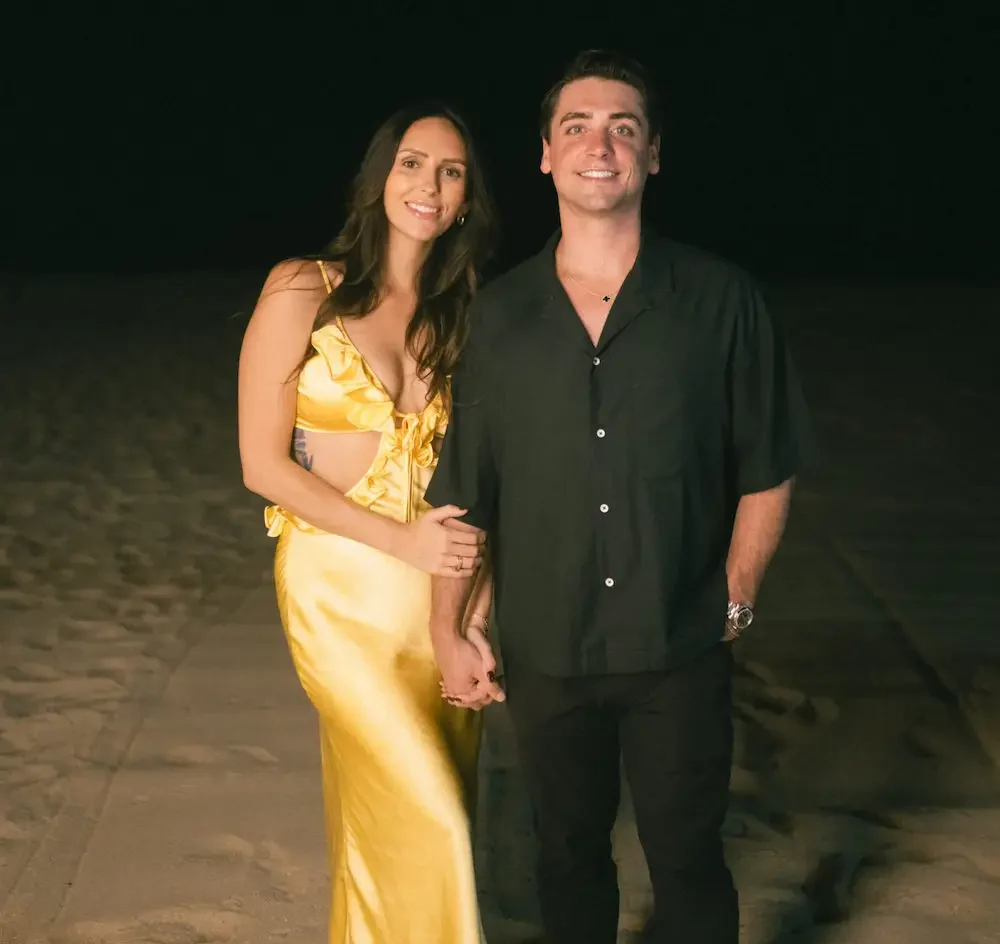 David and Dalis standing together on a beach at night, smiling at the camera